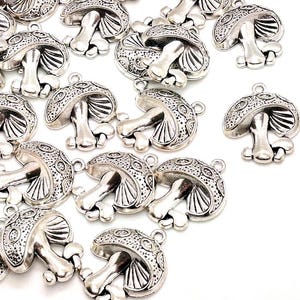 May include: Silver-colored mushroom charms with detailed caps and stems. The charms have a loop for attaching to jewelry or other crafts. The mushroom caps feature an etched design. These charms are ideal for creating unique pendants, earrings, or embellishments.