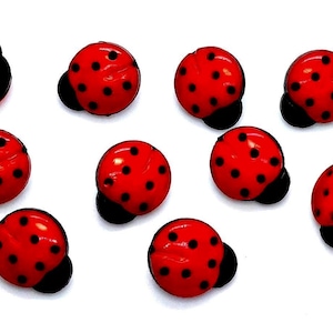 May include: A collection of nine round buttons shaped like ladybugs, featuring a bright red domed surface with black spots and a black base. Each button has a smooth, glossy finish and a distinct circular form resembling the insect's shell.