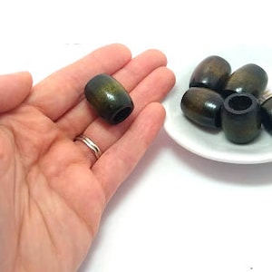 May include: A close-up of a hand holding a dark green wooden bead. There are several more beads in the background, all of the same style.
