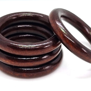 May include: A stack of five dark brown wooden rings with a glossy finish, one ring is separate. The rings are circular and appear to be for a craft project or home decor.