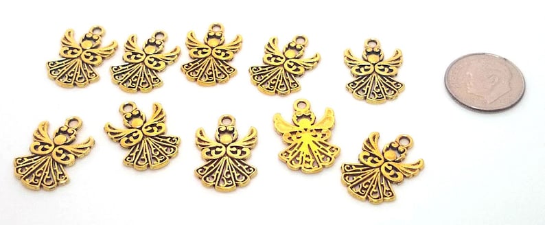 May include: Ten gold-colored angel charms with intricate details. The charms are about the size of a US quarter.