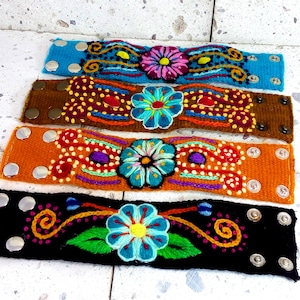 May include: Four colorful embroidered bracelets with floral designs. Each bracelet has a different color base and features a different floral pattern. The bracelets are made of woven fabric and have metal snaps.