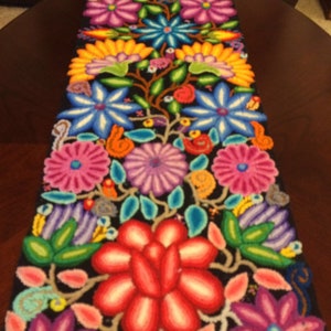 May include: A colorful table runner with a floral design. The runner is black with bright pink, red, yellow, blue, and green flowers.