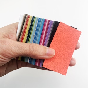 May include: A hand holding a stack of colourful leather swatches. The top swatch is a bright orange colour.