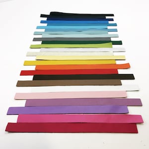 May include: A collection of 17 leather strips in various colours, including black, blue, green, yellow, orange, red, brown, pink, purple, and white. The strips are arranged in a vertical stack, with the darkest colour at the top and the lightest colour at the bottom.