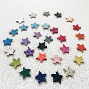 May include: A selection of small, star-shaped leather cutouts in a variety of colours, such as blue, purple, pink, and green. The stars are arranged on a white surface, creating a visually appealing display.