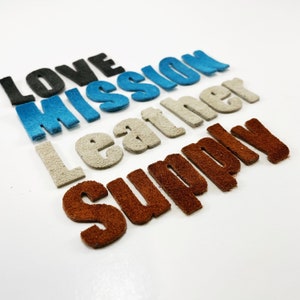 Op de afbeelding: Vijf viltwoorden in verschillende kleuren: "Love", "Mission", "Leather", "Supply" en een bruin woord dat te wazig is om te lezen.