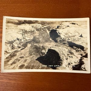 May include: Vintage black and white postcard featuring a landscape view of Coso Hot Springs, CA. The image shows a rugged terrain with water features and the text "COSO HOT SPRINGS, CA" at the bottom.