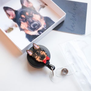 Black work badge reel with clip and clear case with a card slot. Painted wooden German Shepard dog cutout glued to badge reel. Dog has black glasses on and a red bow tie.