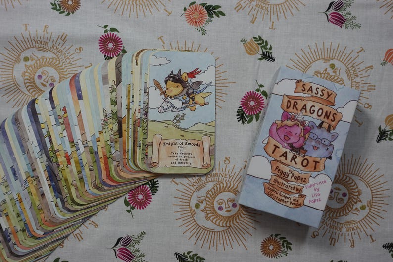 May include: A deck of Sassy Dragons Tarot cards by Peggy Papez, featuring a fan of illustrated cards and a box with the title Sassy Dragons Tarot. The top card shows a dragon knight on a horse with the text Knight of Swords. The cards have rounded corners.