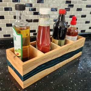 Może przedstawiać: Drewniany stojak na przyprawy z czterema przegródkami, z wkładką z turkusowej żywicy. Stojak jest wypełniony czterema butelkami różnych sosów i olejów.
