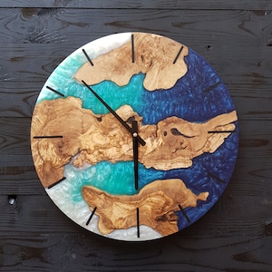Könnte beinhalten: Eine runde Uhr mit weißem Hintergrund und blauen und grünen Harzakzenten. Das Zifferblatt der Uhr ist aus Holz mit natürlicher Maserung. Die Zeiger der Uhr sind schwarz.