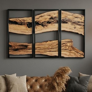 Może przedstawiać: Scena w salonie z brązową skórzaną sofą, poduszkami i drewnianym stolikiem kawowym. Nad sofą tryptyk z drewnianej sztuki w czarnych ramach. Wisząca lampa i roślina doniczkowa dopełniają wystroju.