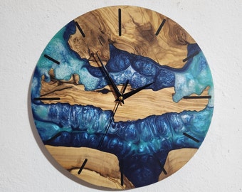 Può includere: Un orologio rotondo in legno con un'intarsio in resina blu e verde. Il quadrante dell'orologio ha lancette nere e un centro dorato.