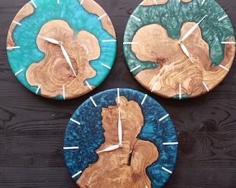 May include: Three round wall clocks with a wood base and blue and green resin accents. The clocks have white hands and white markings for the hours.