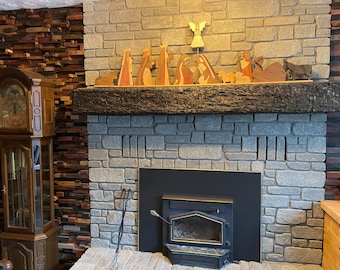 May include: A gray brick fireplace with a black wood-burning stove. A wooden mantelpiece above the fireplace is decorated with a nativity scene featuring wooden figurines of the baby Jesus, Mary, Joseph, angels, and animals.