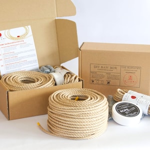 Op de afbeelding: Een DIY Raw Box-kit met natuurlijk gekleurd touw, touwboter en instructies. De kit bevat een grote rol touw, kleinere bundels en een witte container met touwboter. De doos is open en onthult de inhoud.