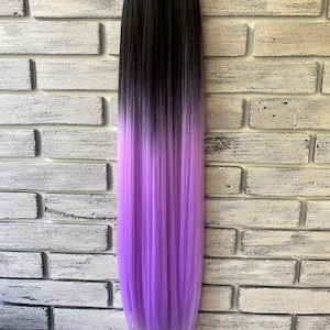 Può includere: Un fascio di extension per capelli sintetici sfumate dal nero al viola. I capelli sono lisci e passano dal nero nella parte superiore a un viola vibrante nella parte inferiore. Le extension sono attaccate a un elastico nero.