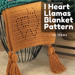 May include: A crocheted blanket with a heart pattern in a mustard yellow color. The blanket has tassels on the bottom and is folded on top of other blankets in pink and teal. The text "I Heart Llamas Blanket Pattern" is written in black on a white background. The text "UK TERMS" is written in black on a white background.