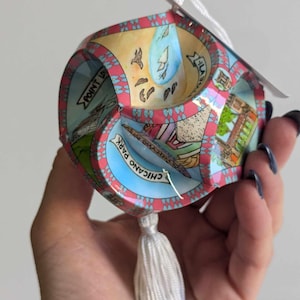 Op de afbeelding: Een veelzijdige, kleurrijke papieren ornament met een witte kwast. De ornament toont een kaart van een stad met de zichtbare woorden "Chicano Park" en "Point Loma".