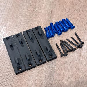 Pu&ograve; includere: Un kit hardware con quattro staffe di montaggio nere, tasselli blu e viti nere. Le staffe sono rettangolari con un gancio e un foro per le viti. Le viti e i tasselli sono disposti accanto alle staffe.