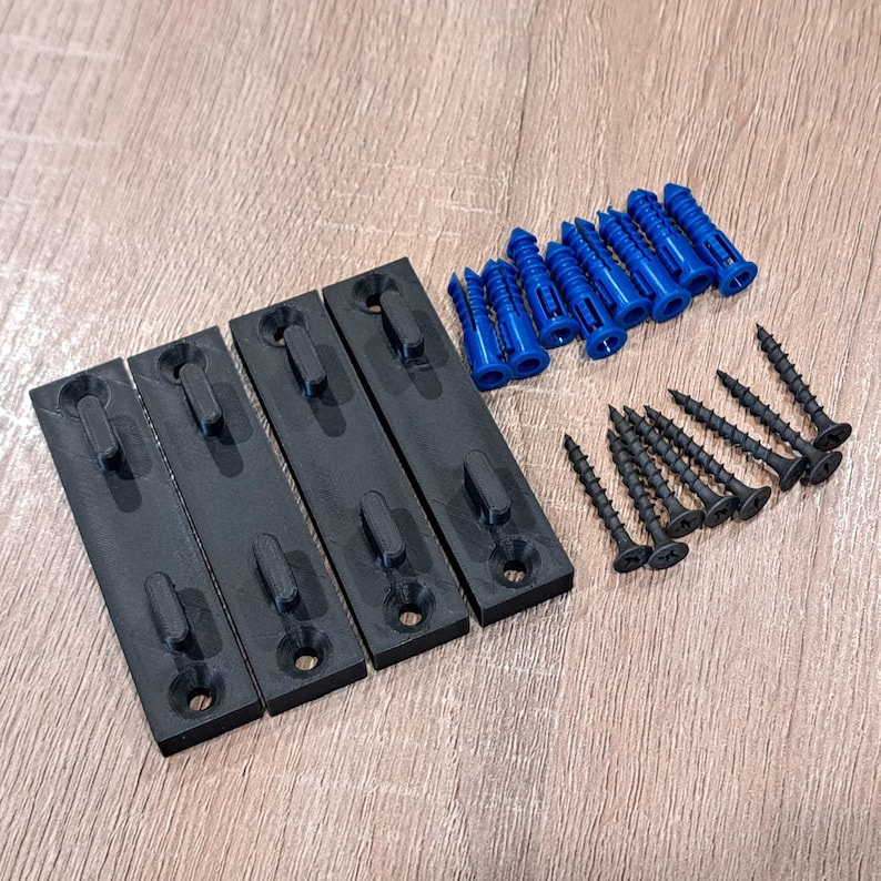 Pu&ograve; includere: Un kit hardware con quattro staffe di montaggio nere, tasselli blu e viti nere. Le staffe sono rettangolari con un gancio e un foro per le viti. Le viti e i tasselli sono disposti accanto alle staffe.