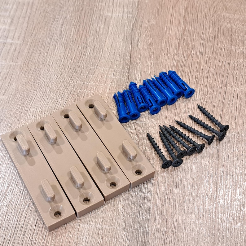 Pu&ograve; includere: Un kit hardware con quattro staffe di montaggio beige, tasselli blu e viti nere. Le staffe hanno una forma rettangolare con un elemento ovale in rilievo e un foro per il montaggio. Le viti sono lunghe circa 2,5 cm.