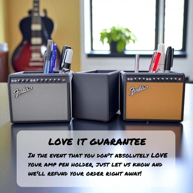 May include: Three pen holders designed to resemble guitar amplifiers. The pen holders are black with silver and orange speaker grilles. The Fender logo is visible on the front of the two amp-style holders. Pens and markers are inside the holders.