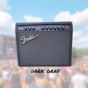 May include: Dark gray Fender guitar amplifier with a speaker grill and control knobs. The Fender logo is visible on the front. The text "DARK GRAY" is at the bottom of the image. The background is a blurred image of a crowd and a blue sky.