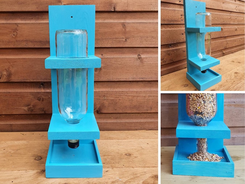 May include: A blue wooden bird feeder with a clear glass bottle for holding birdseed. The feeder has two shelves and a tray at the bottom for catching spilled seed.