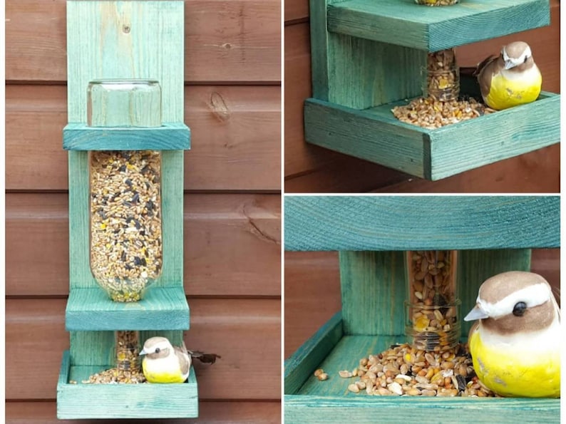 May include: A teal blue wooden bird feeder with two platforms. The feeder has a clear glass bottle in the center with birdseed inside. A small yellow bird figurine is perched on the bottom platform.