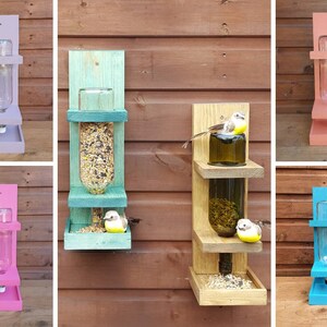 May include: Six different bird feeders made from wood and glass bottles. The feeders are painted in various colors, including purple, pink, teal, blue, and natural wood. Each feeder has a platform for birds to perch on and a clear glass bottle for holding birdseed.