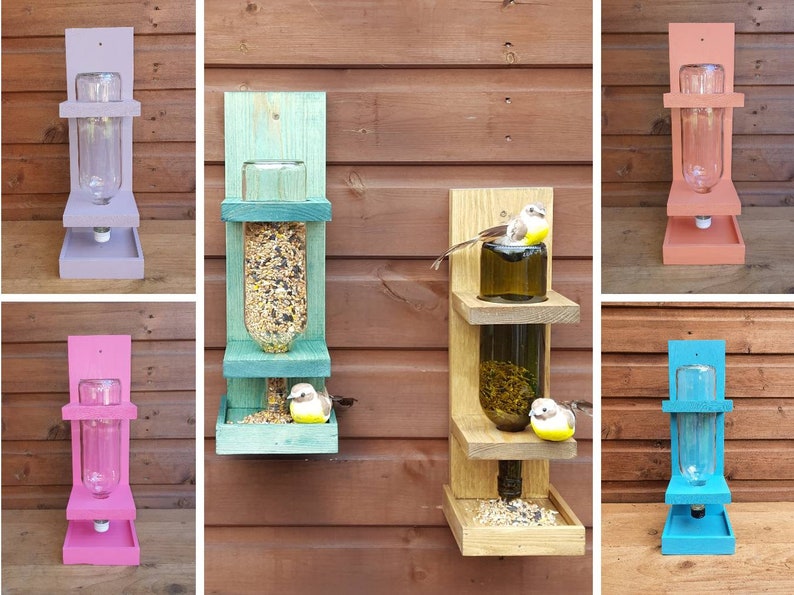 May include: Six different bird feeders made from wood and glass bottles. The feeders are painted in various colors, including purple, pink, teal, blue, and natural wood. Each feeder has a platform for birds to perch on and a clear glass bottle for holding birdseed.