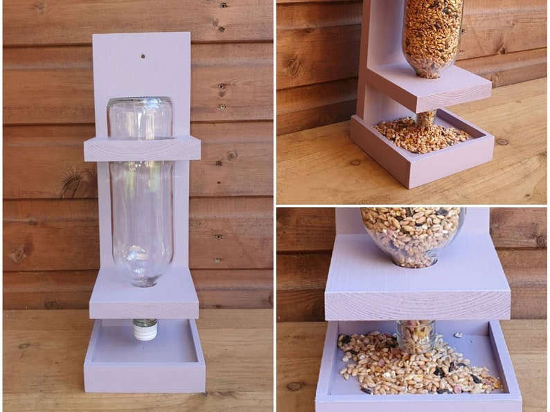 May include: Purple wooden bird feeder with two platforms. The top platform has a clear glass bottle for holding birdseed. The bottom platform has a tray for catching spilled seed.