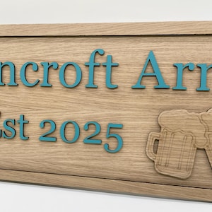 K&ouml;nnte beinhalten: Ein Holzschild mit dem Text "Lincroft Arms Est 2025" in blaugr&uuml;ner Schrift. Das Schild zeigt zwei erhabene, geschnitzte Bierkr&uuml;ge aus Holz mit Schaumkronen.