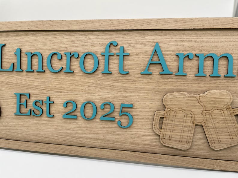 K&ouml;nnte beinhalten: Ein Holzschild mit dem Text "Lincroft Arms Est 2025" in blaugr&uuml;ner Schrift. Das Schild zeigt zwei erhabene, geschnitzte Bierkr&uuml;ge aus Holz mit Schaumkronen.