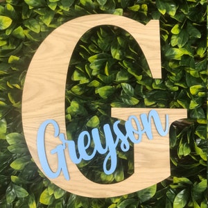 May include: A wooden letter G with the name Greyson written in light blue cursive lettering.