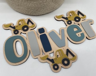 May include: A wooden name sign spelling "Oliver" with a construction theme. Each letter is a different colour, with a yellow excavator on the top and bottom. The letters are mounted on a light wood base.