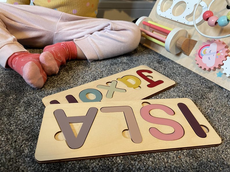 Puede incluir: Dos tableros de rompecabezas de madera con los nombres "ISLA" y "JAXON" deletreados en letras de colores. Las letras est&aacute;n recortadas y encajan en los tableros de rompecabezas.