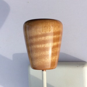 May include: A wooden knob with a glossy finish, featuring a light brown color with visible wood grain. The knob is mounted on a white metal rod. The knob has a rounded, tapered shape.