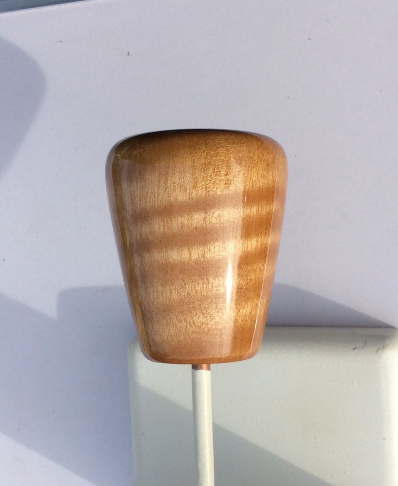 May include: A wooden knob with a glossy finish, featuring a light brown color with visible wood grain. The knob is mounted on a white metal rod. The knob has a rounded, tapered shape.