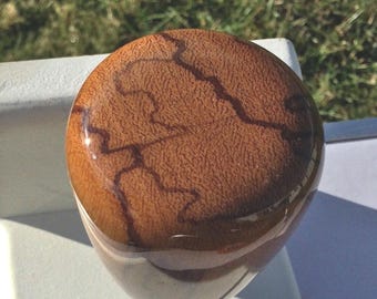 May include: A brown, globe-shaped wooden shift knob with a glossy finish. The top surface has a textured appearance with darker brown, vein-like patterns. The knob is mounted on a white stem, suggesting a car interior accessory.