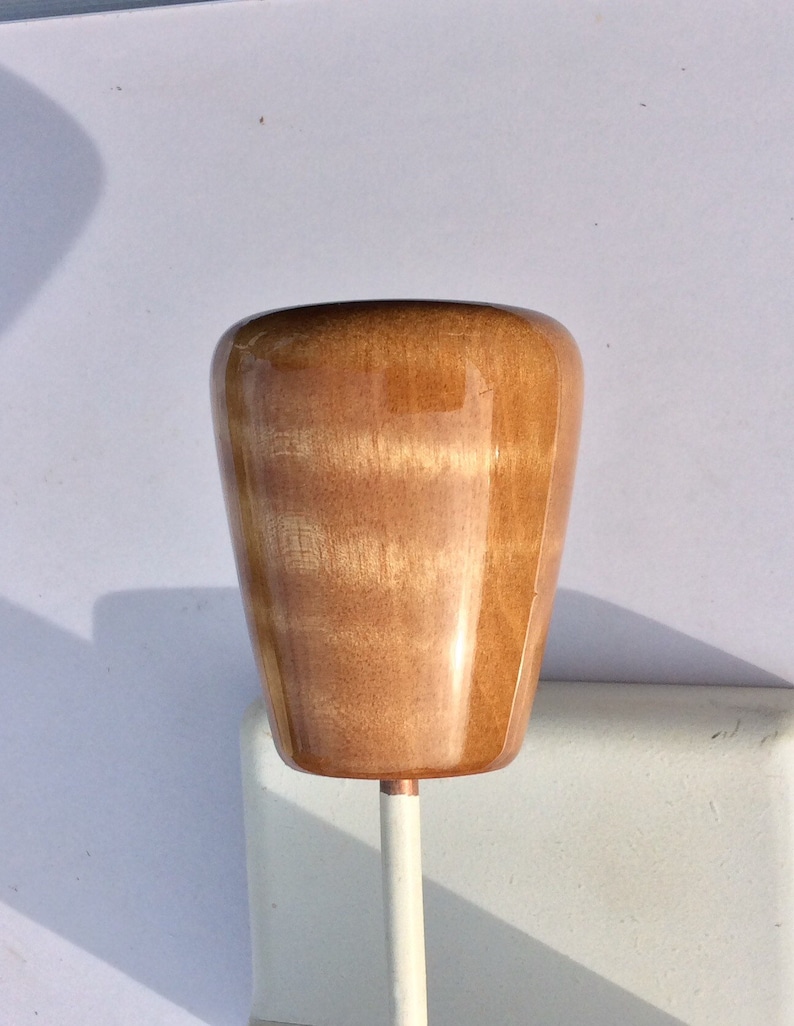 May include: A wooden knob with a glossy finish, featuring a light brown color with visible wood grain. The knob is mounted on a white metal rod. The knob's shape is a rounded, inverted cone.