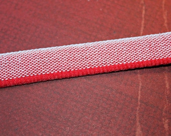 May include: A close-up of a red and white woven ribbon. The ribbon has a textured surface and is made of a soft material.