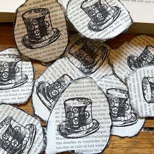 Könnte beinhalten: Zehn Papierschnitte mit einer Schwarzweißillustration eines Zylinders mit Zahnrädern. Die Zylinder sind auf Seiten eines Buches mit deutschem Text gedruckt.