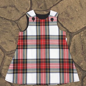 Puede incluir: Un vestido sin mangas de cuadros blancos, rojos y negros con botones negros. El vestido tiene un forro negro.