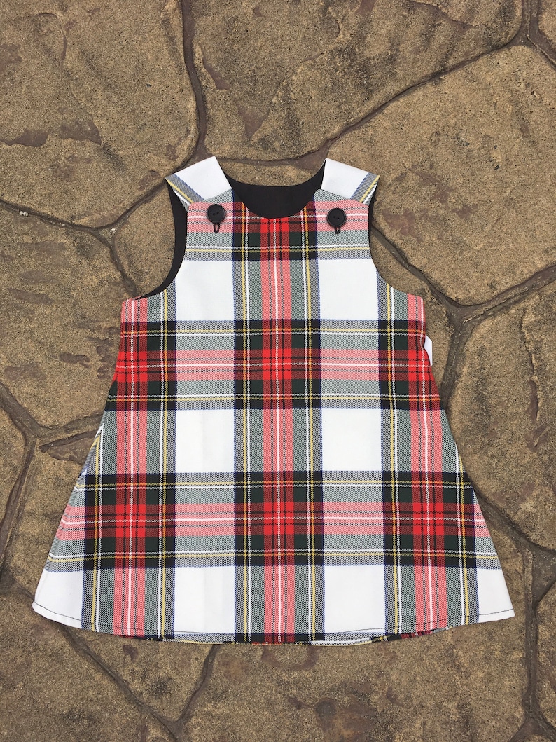 Puede incluir: Un vestido sin mangas de cuadros blancos, rojos y negros con botones negros. El vestido tiene un forro negro.