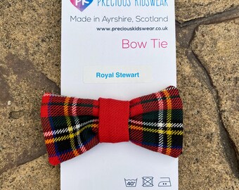 May include: A red and black plaid bow tie with a red center. The bow tie is made of 65% polyester and 35% viscose. The label says "PK Precious Kidswear" and "Royal Stewart".