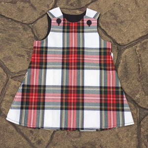 Puede incluir: Un vestido sin mangas de cuadros blancos, rojos y negros con cuello negro y dos botones negros.