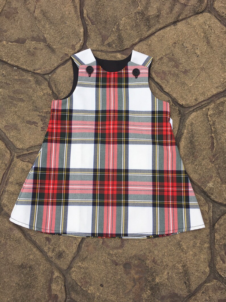 Puede incluir: Un vestido sin mangas de cuadros blancos, rojos y negros con cuello negro y dos botones negros.